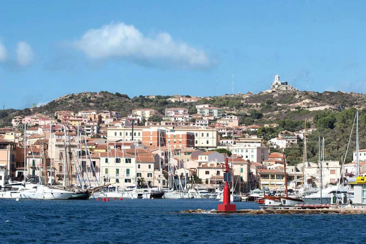Sentiero panoramico tra la macchia mediterranea di Caprera che conduce a una caletta dall’acqua trasparente, presenza di qualche escursionista con zaino